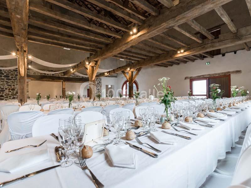 Salle de réception avec tables dressées, nappes blanches, couverts alignés et décorations florales.