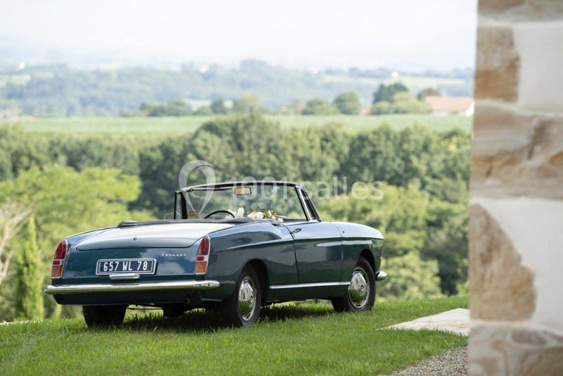 Voiture décapotable ancienne bleue stationnée sur une pelouse, avec un paysage rural en arrière-plan.