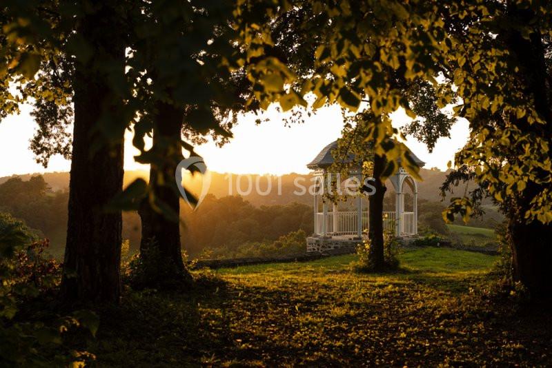 Un kiosque en bois au coucher du soleil, entouré d'arbres et donnant sur un paysage vallonné verdoyant.