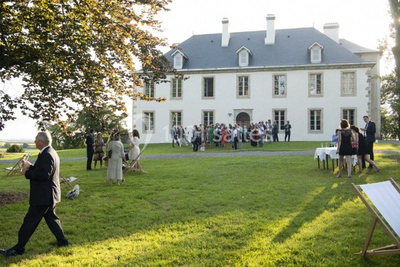 Groupe de personnes rassemblées devant une grande maison blanche dans un jardin verdoyant par temps ensoleillé.