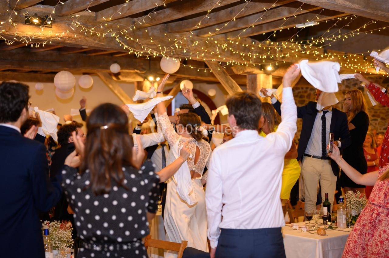 Des invités célèbrent en levant des serviettes dans une salle décorée de guirlandes lumineuses et de lanternes suspendues.