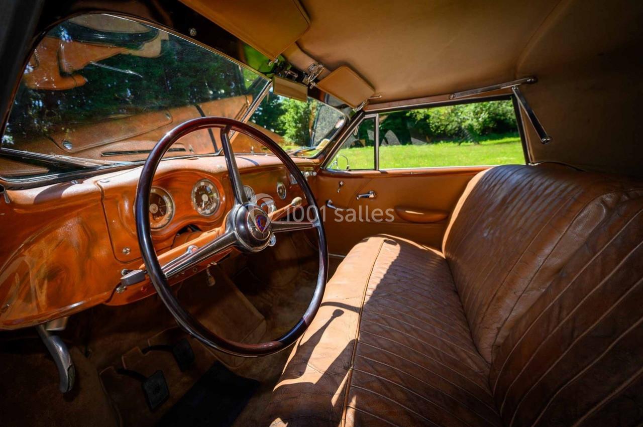 Intérieur d'une voiture ancienne avec sièges en cuir marron, volant en bois et tableau de bord rétro.