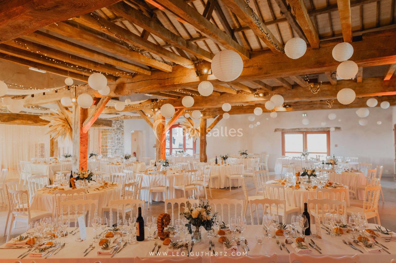 Salle de réception décorée pour un mariage, avec tables dressées, guirlandes lumineuses et lanternes suspendues.