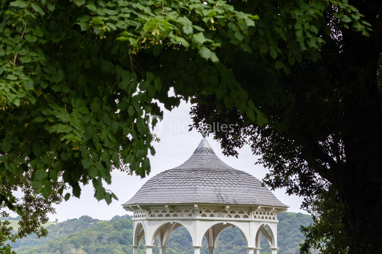 Kiosque blanc en bois au toit arrondi, entouré de verdure, avec une vue dégagée sur des collines boisées.