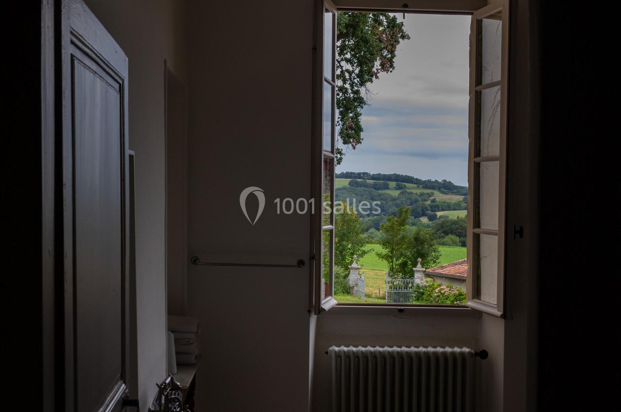 Salle de bain sombre avec une baignoire sur pieds, une fenêtre ouverte donnant sur un paysage verdoyant.