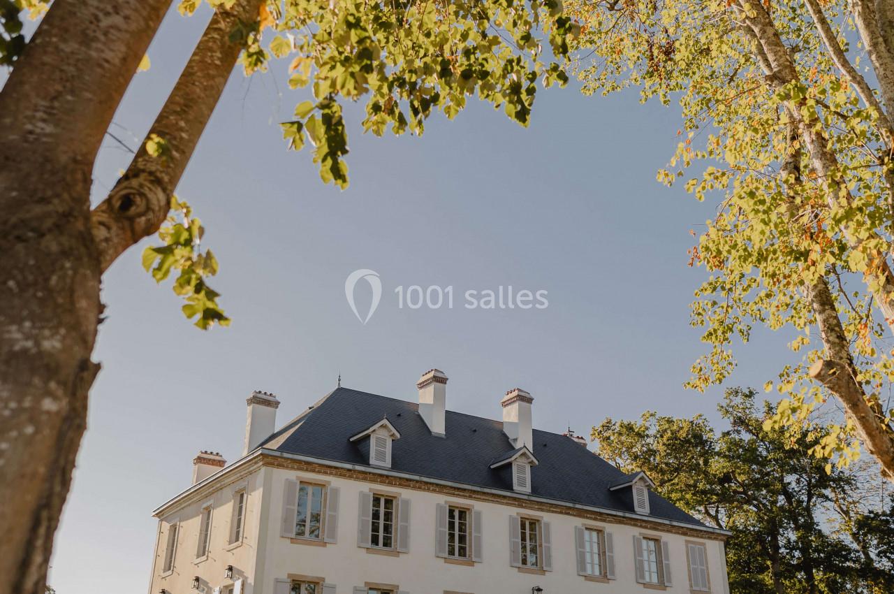 Façade d'un manoir blanc entouré d'arbres, situé sur une pelouse sous un ciel dégagé.