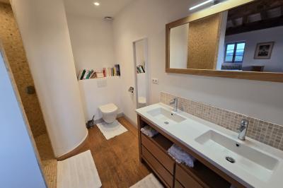 Chambre lumineuse avec poutres apparentes, lit double, commode en bois et fenêtres donnant sur l'extérieur.