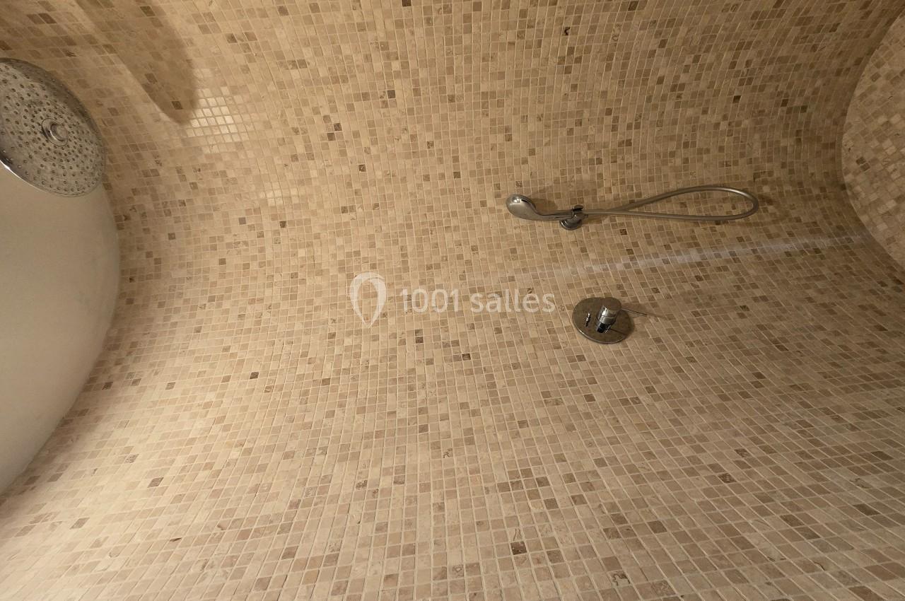 Douche avec murs et plafond recouverts de mosaïques beige, équipée d'une pomme de douche et d'un mitigeur.