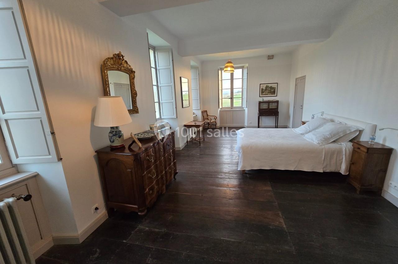 Chambre lumineuse avec lit double, meubles en bois, parquet sombre et grandes fenêtres donnant sur l'extérieur.