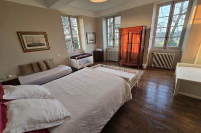 Chambre lumineuse avec poutres apparentes, lit double, commode en bois et fenêtres donnant sur l'extérieur.