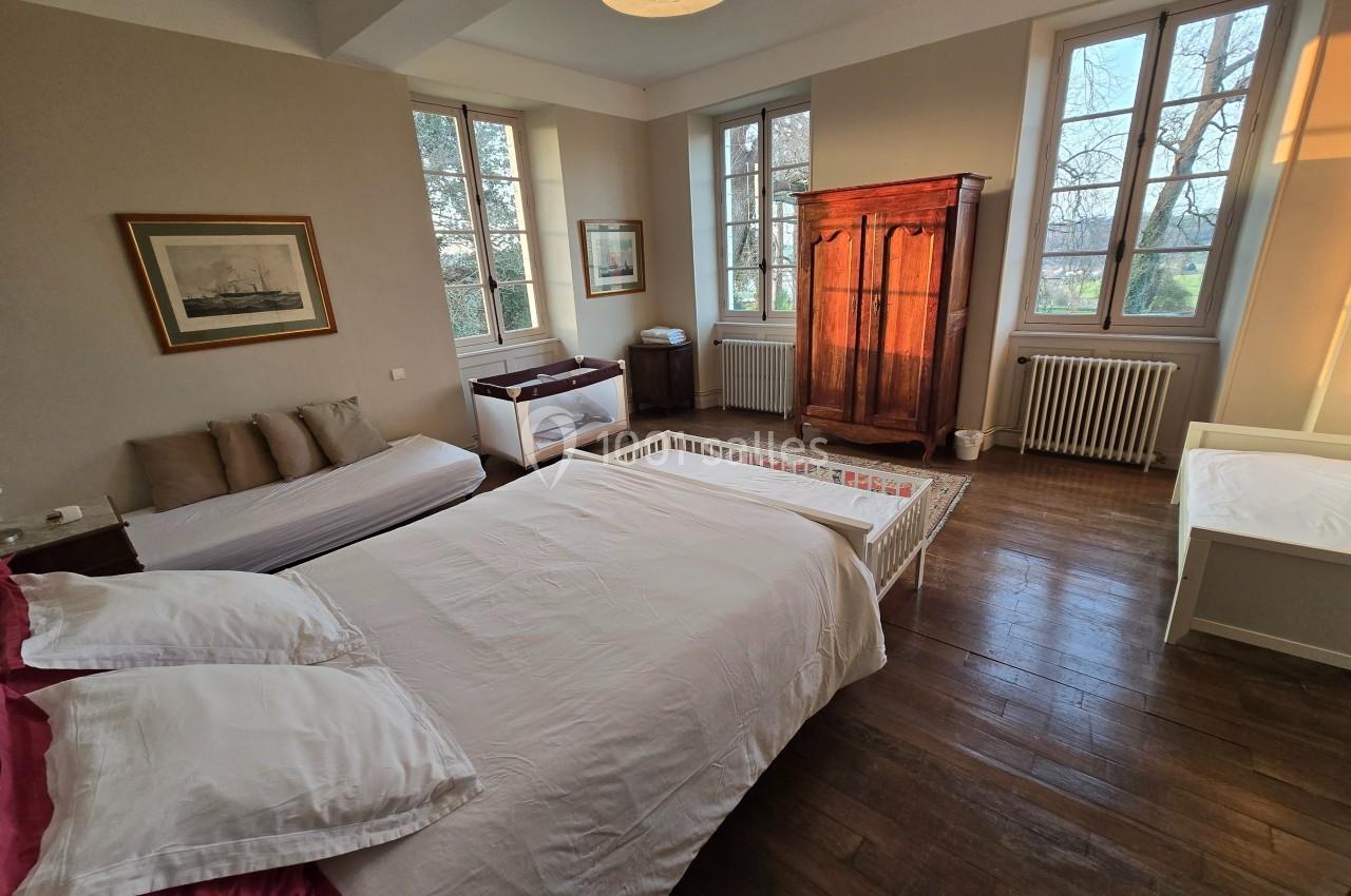 Chambre lumineuse avec lit double, lit bébé, armoire en bois, canapé et grandes fenêtres donnant sur l'extérieur.