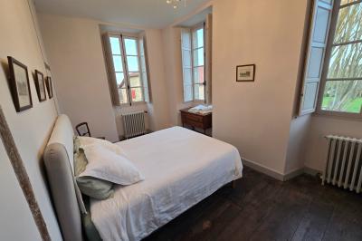 Chambre lumineuse avec poutres apparentes, lit double, commode en bois et fenêtres donnant sur l'extérieur.