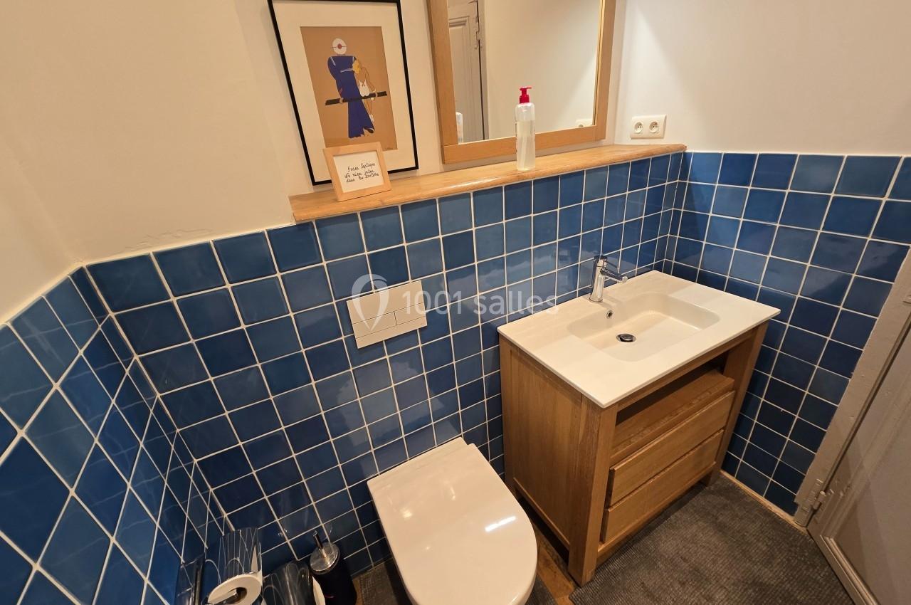 Toilettes modernes avec carrelage bleu, meuble-lavabo en bois, miroir, et décoration murale encadrée.