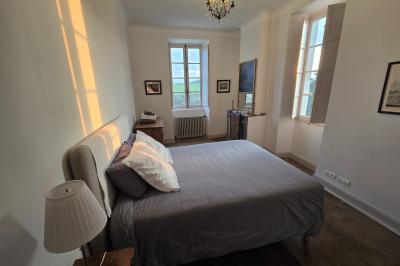 Chambre lumineuse avec poutres apparentes, lit double, commode en bois et fenêtres donnant sur l'extérieur.
