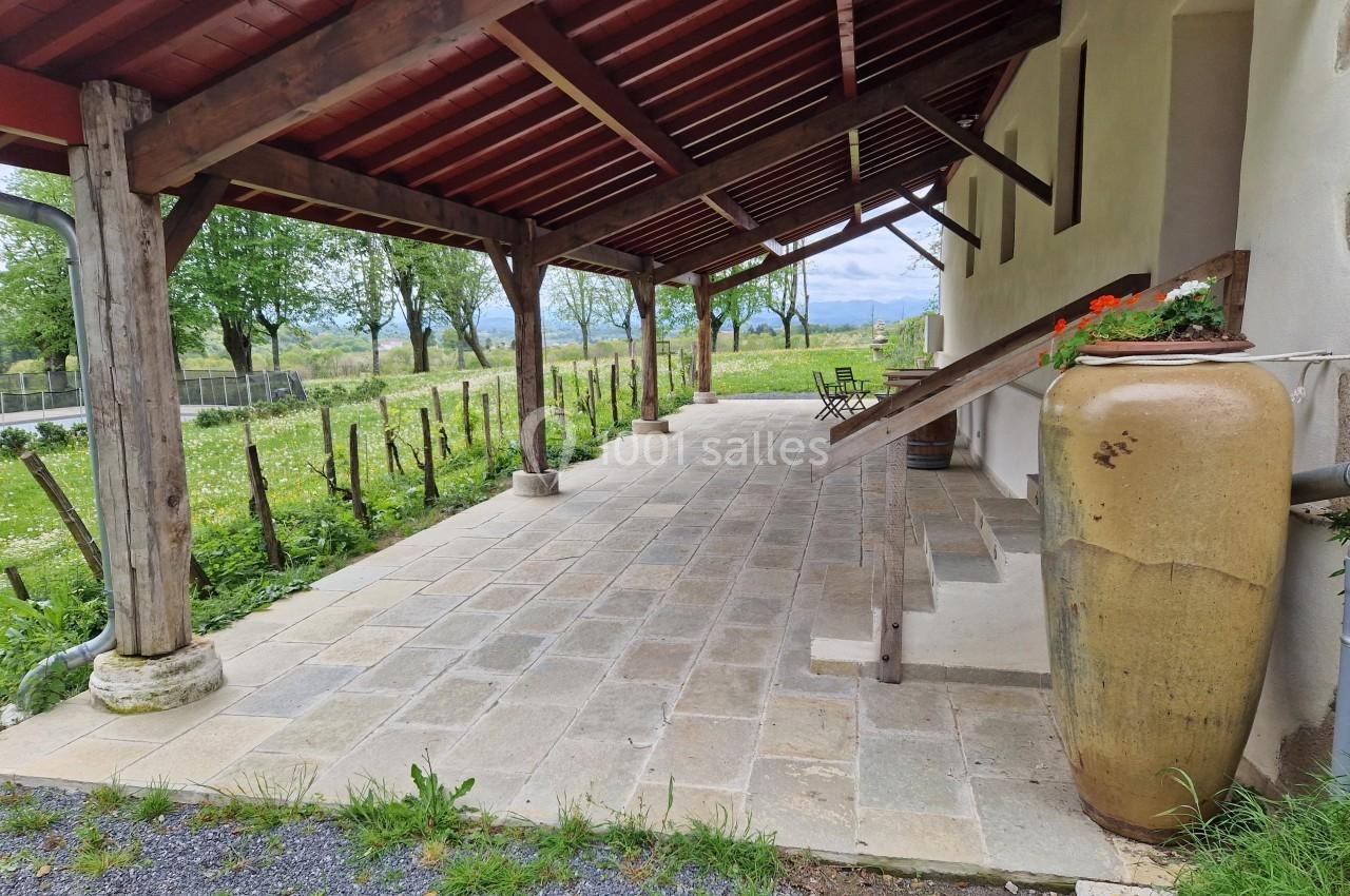 Terrasse couverte en bois avec sol en pierre, grande jarre décorative et vue sur un jardin verdoyant.