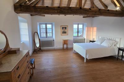 Chambre lumineuse avec poutres apparentes, lit double, commode en bois et fenêtres donnant sur l'extérieur.