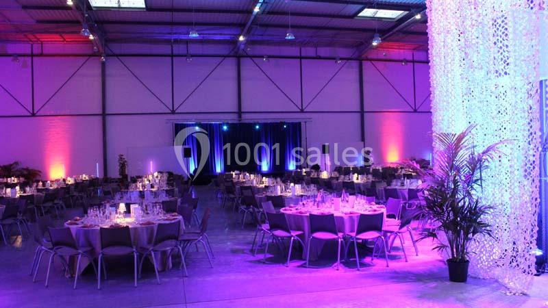 Salle de réception décorée avec des tables dressées, éclairage coloré et rideaux lumineux en arrière-plan.