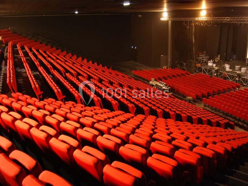 Rangées de fauteuils rouges alignées dans une grande salle de spectacle vide avec une scène en arrière-plan.