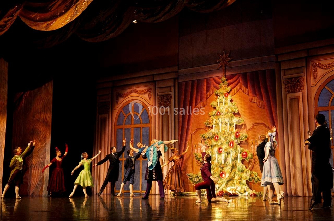 Des danseurs en costume exécutent une scène de ballet devant un grand sapin de Noël décoré sur une scène de théâtre.