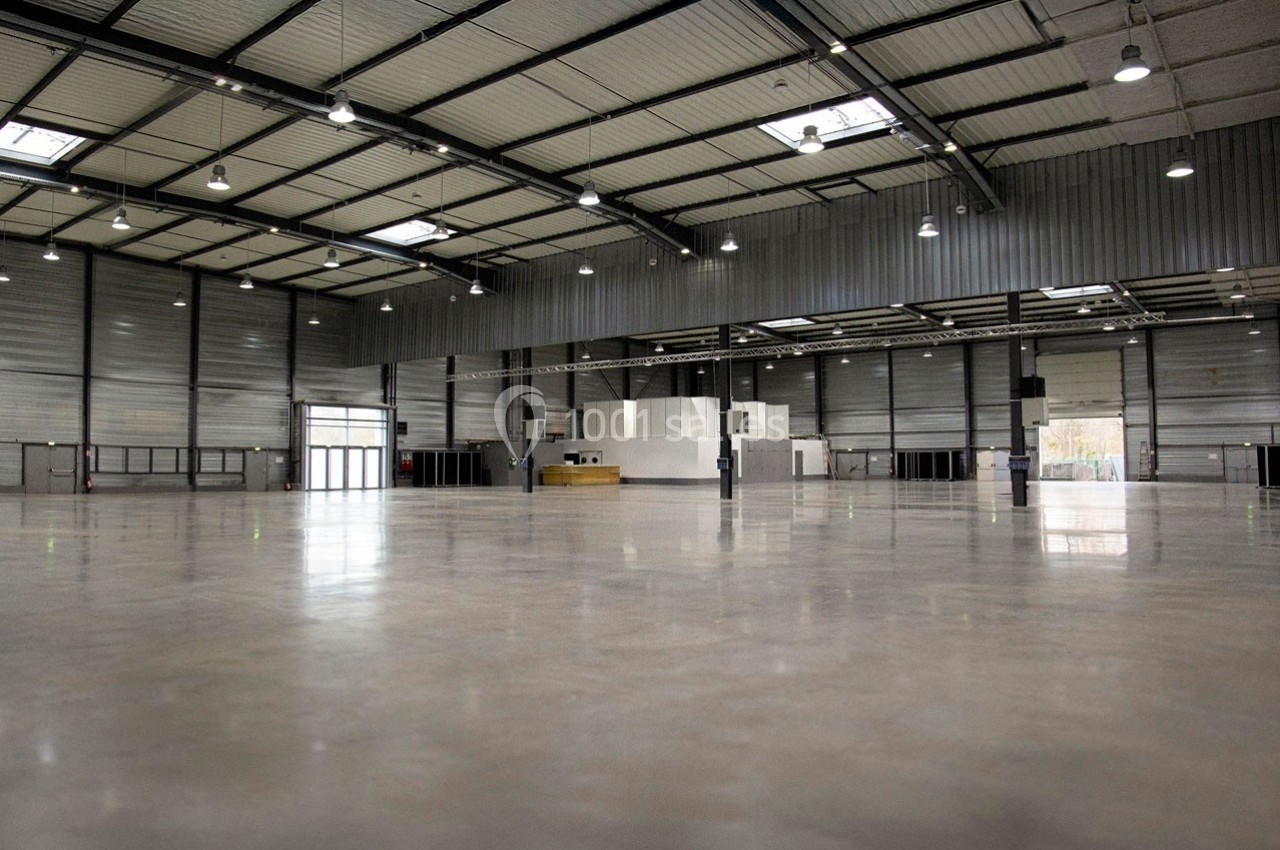 Intérieur d'un grand entrepôt vide avec sol en béton poli, murs métalliques et éclairage suspendu.
