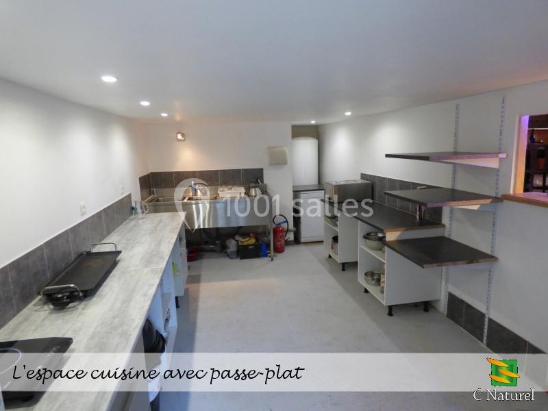 Cuisine fonctionnelle avec passe-plat, équipée d'un évier inox, étagères ouvertes et plan de travail.