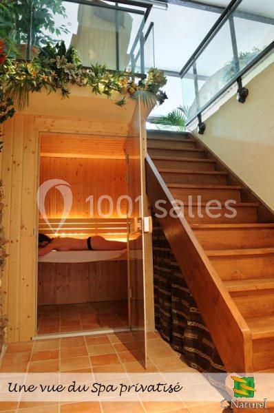 Vue intérieure d'un spa privatisé avec une cabine en bois, une personne allongée et un escalier menant à un étage supérieur.