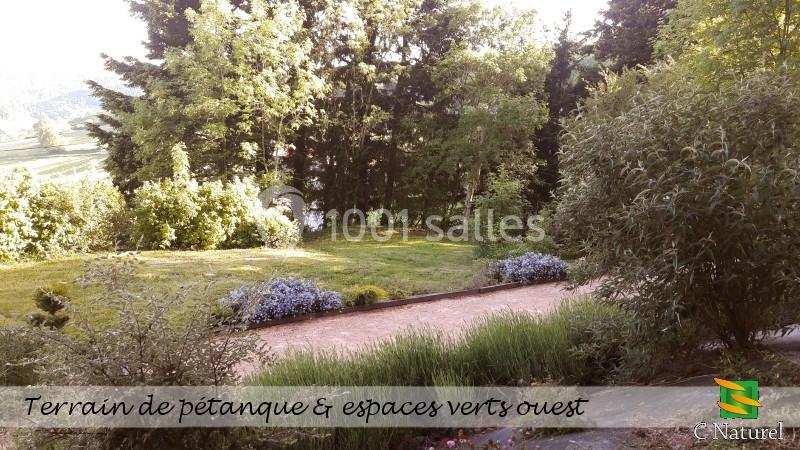 Terrain de pétanque entouré de végétation dense et d'espaces verts arborés.