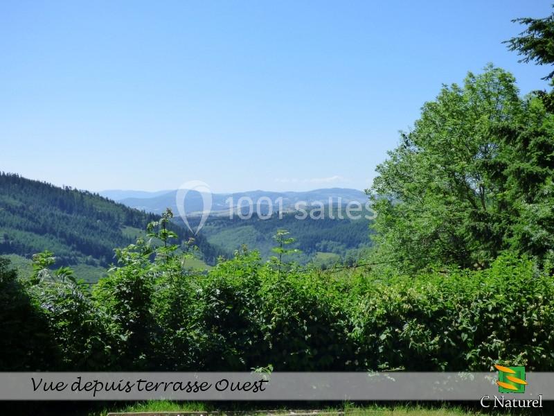 Paysage vallonné avec collines verdoyantes, arbres et ciel dégagé, vu depuis une terrasse entourée de végétation.
