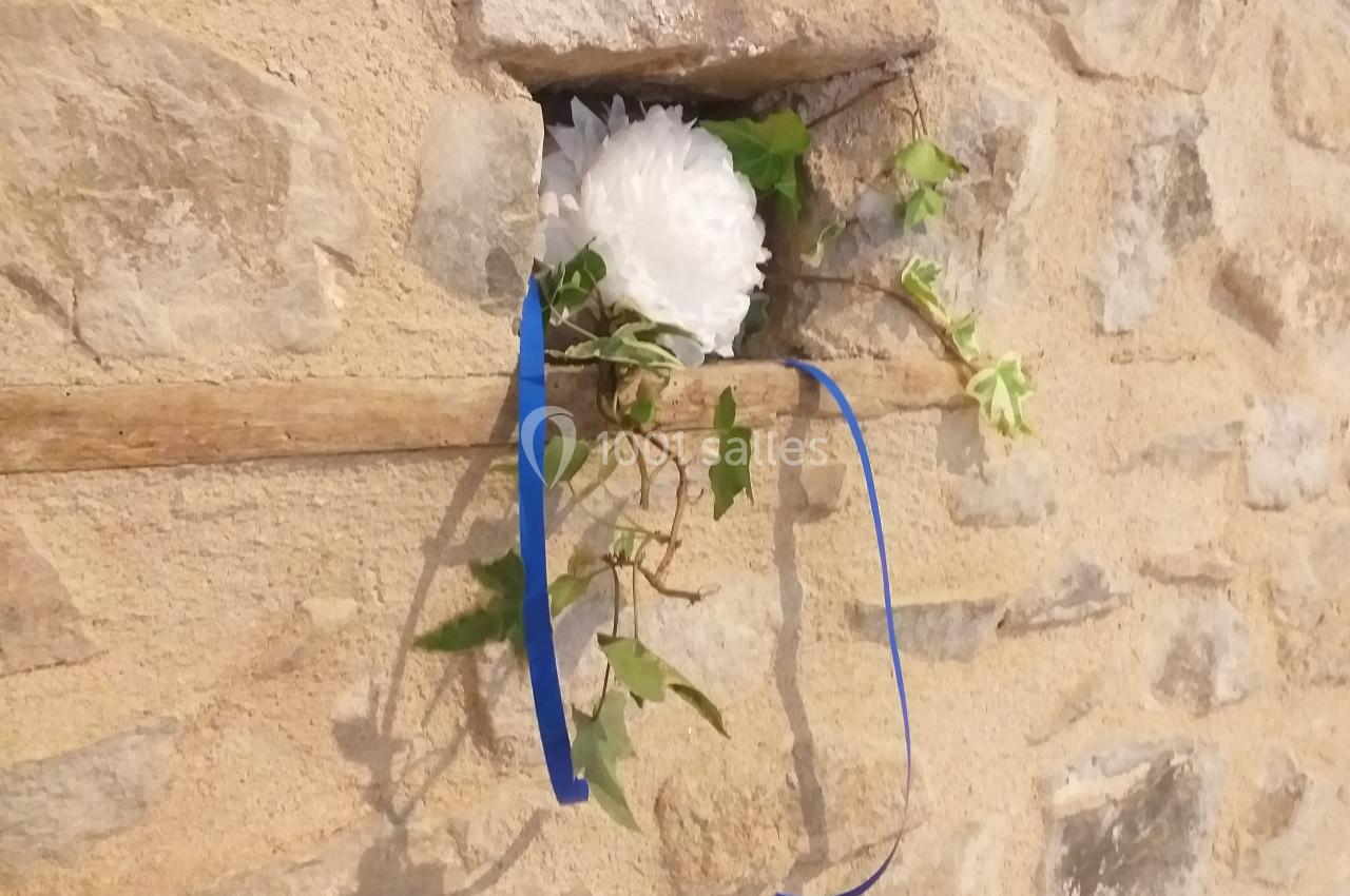 Fleur blanche et lierre avec un ruban bleu insérés dans une ouverture d'un mur en pierre.