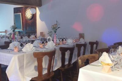Table en bois décorée pour un repas festif, avec bougies, fleurs et vaisselle, dans une salle aux murs en pierre.