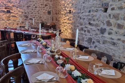 Table en bois décorée pour un repas festif, avec bougies, fleurs et vaisselle, dans une salle aux murs en pierre.