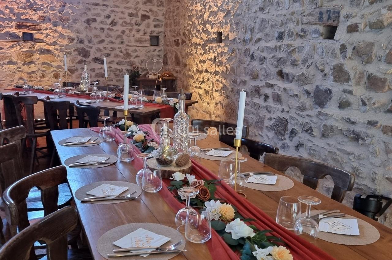 Table en bois décorée pour un repas festif, avec bougies, fleurs et vaisselle, dans une salle aux murs en pierre.