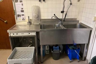 Réfrigérateur professionnel ouvert avec plusieurs étagères métalliques vides dans un environnement de cuisine.