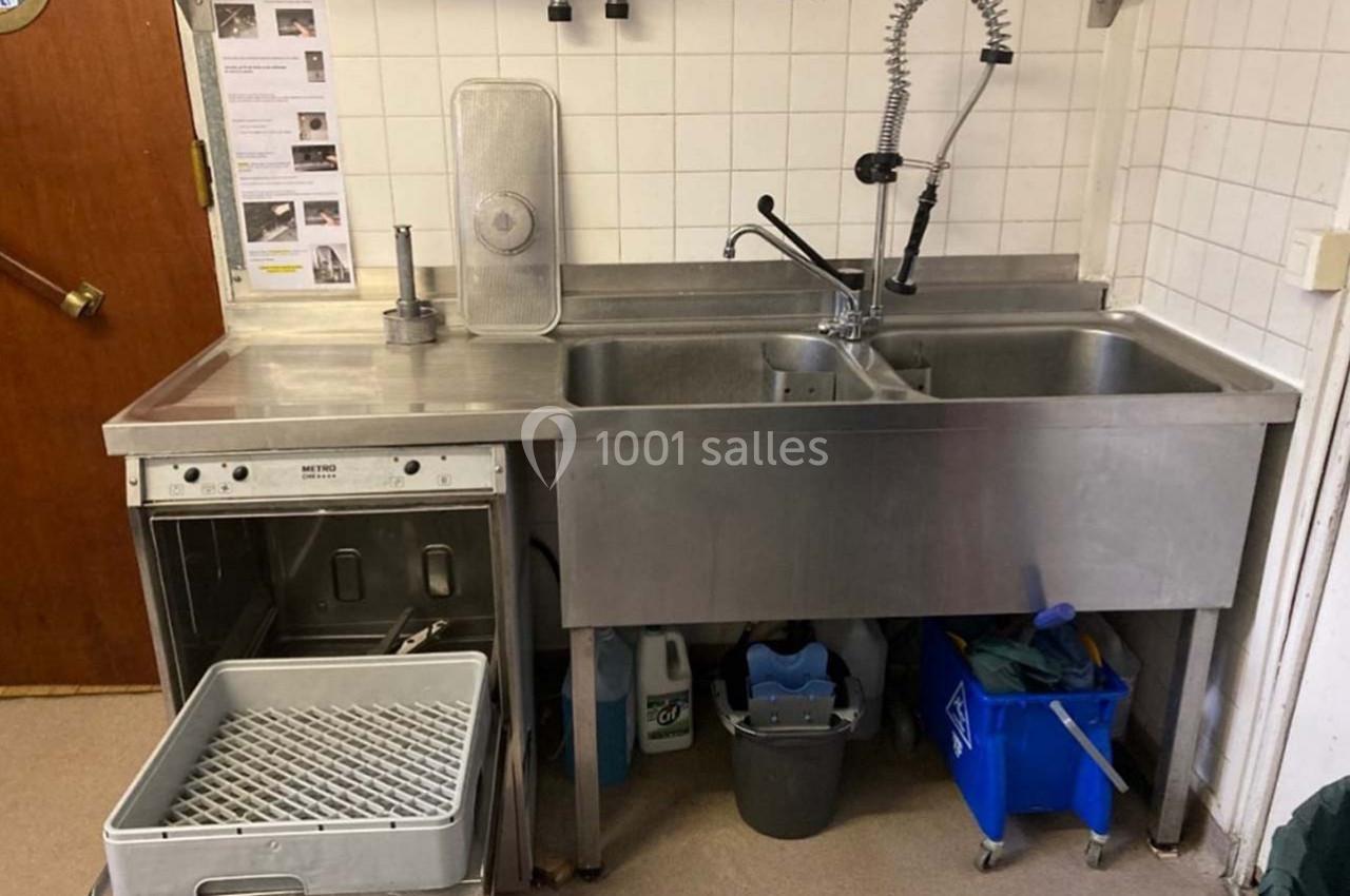 Évier double en acier inoxydable avec robinet flexible, lave-vaisselle ouvert et produits de nettoyage en dessous.