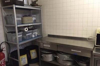 Réfrigérateur professionnel ouvert avec plusieurs étagères métalliques vides dans un environnement de cuisine.