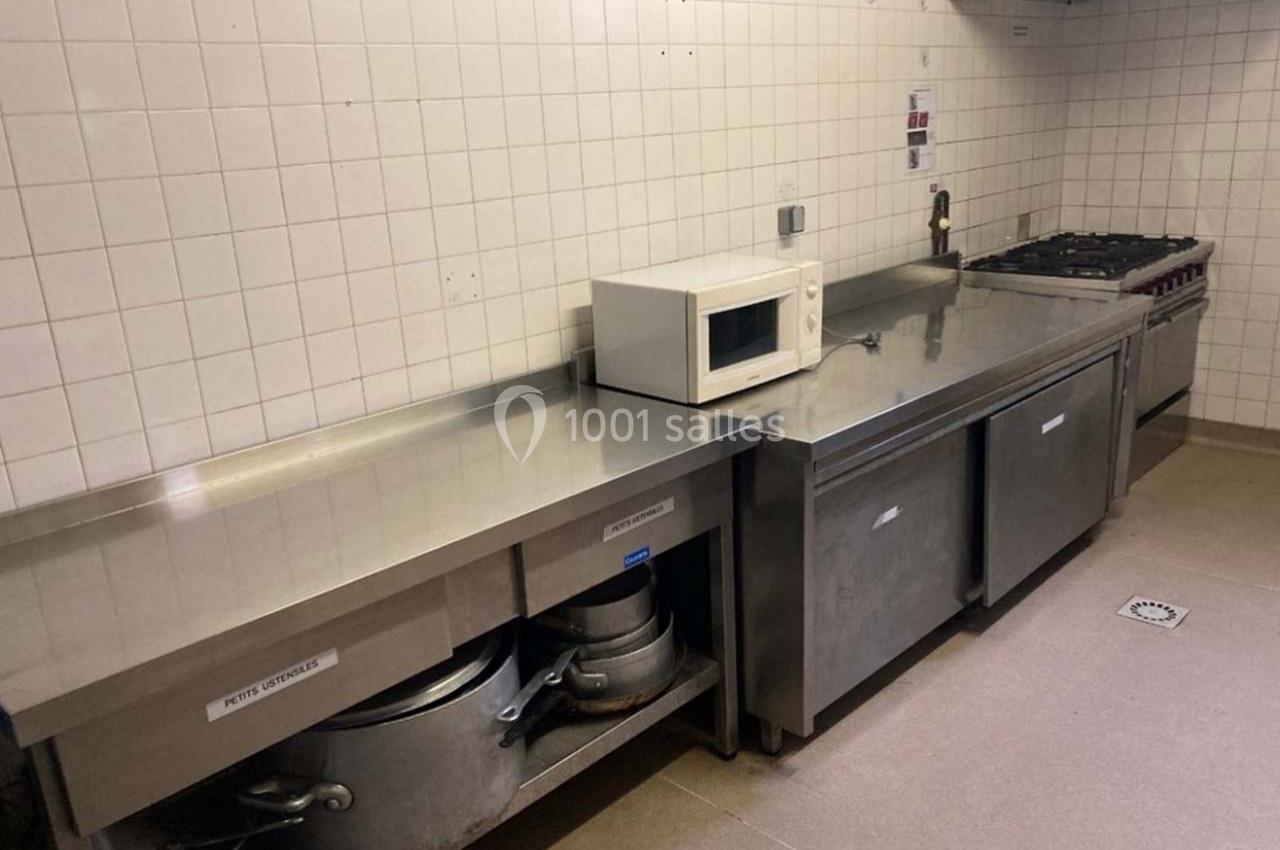 Cuisine professionnelle avec plan de travail en inox, micro-ondes, plaques de cuisson et équipements de rangement.