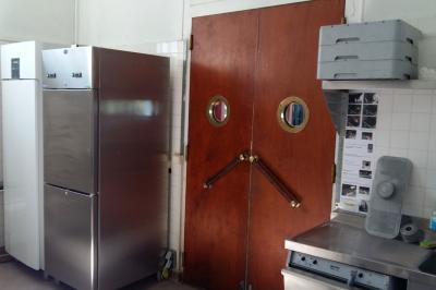 Réfrigérateur professionnel ouvert avec plusieurs étagères métalliques vides dans un environnement de cuisine.