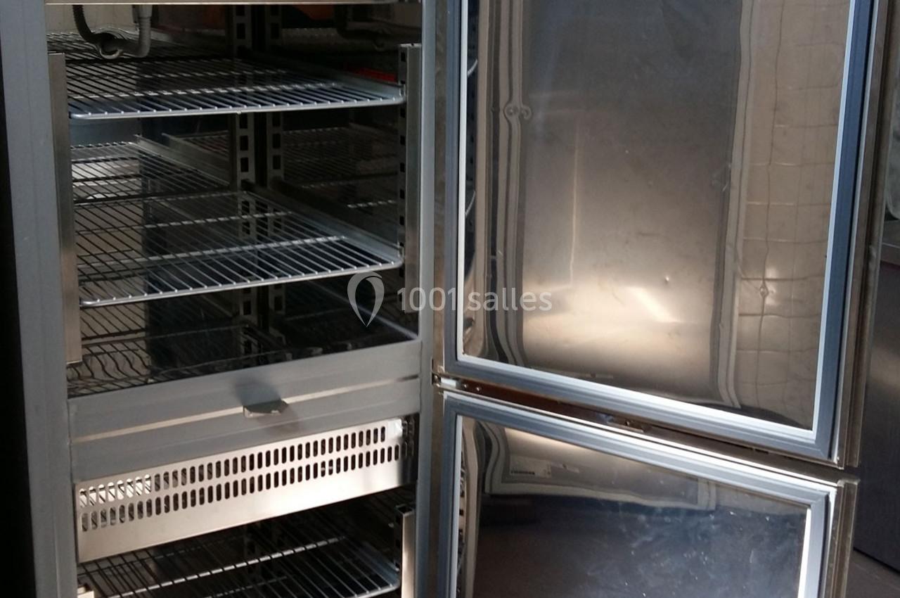 Réfrigérateur professionnel ouvert avec plusieurs étagères métalliques vides dans un environnement de cuisine.