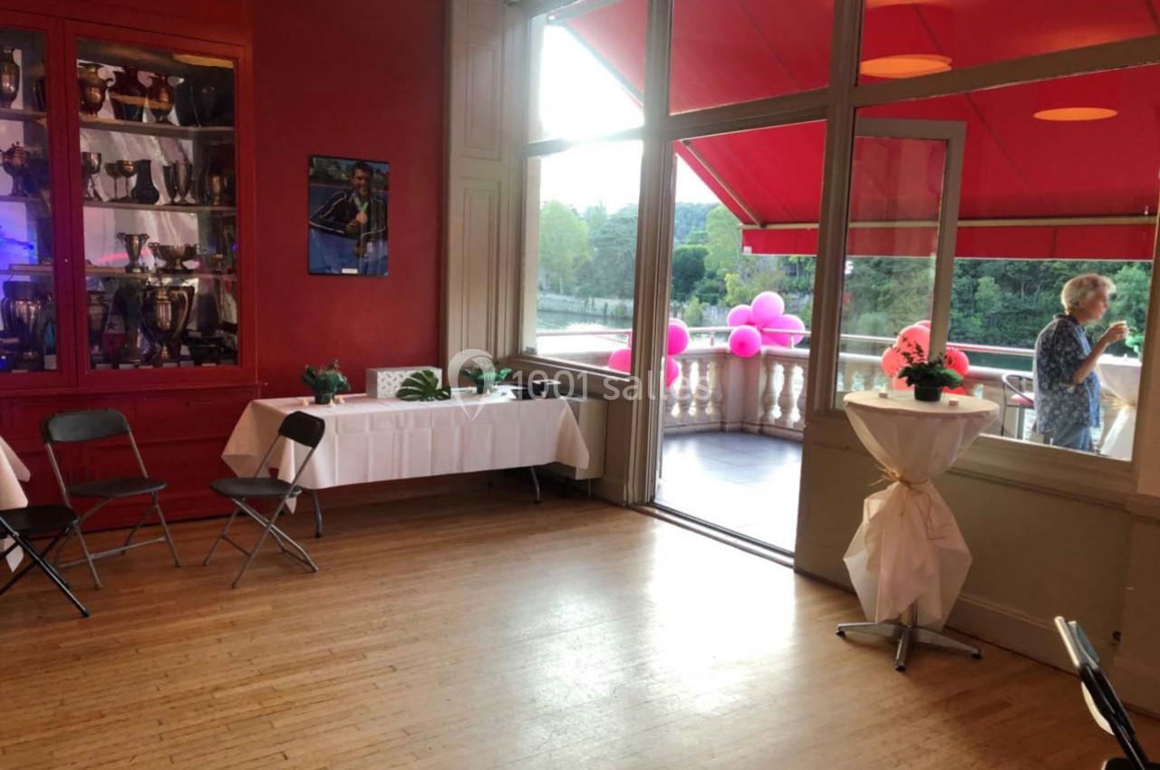 Salle lumineuse avec parquet, tables décorées, baies vitrées ouvertes sur une terrasse avec vue sur un espace verdoyant.