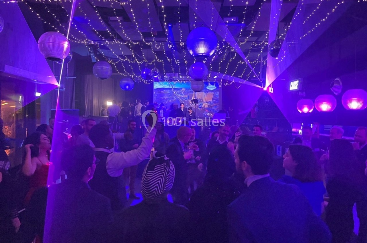 Personnes dansant sous des lumières colorées et des décorations suspendues dans une salle de fête animée.