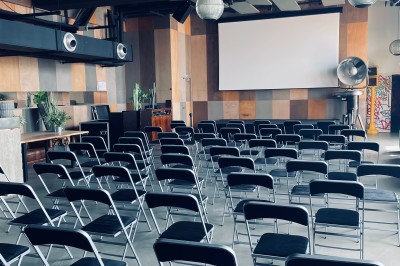 Salle de conférence moderne avec des chaises pliantes alignées face à un écran de projection.