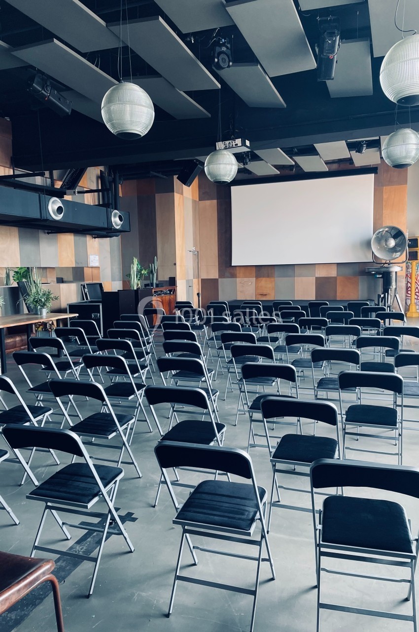 Salle de conférence moderne avec des chaises pliantes alignées face à un écran de projection.