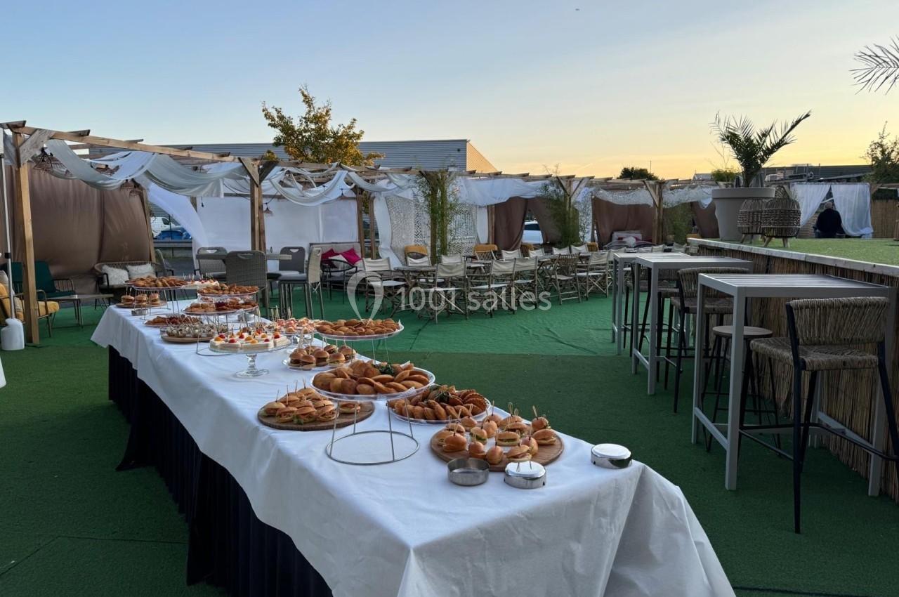 Buffet en extérieur avec tables dressées, chaises et décoration blanche sous un ciel au coucher du soleil.