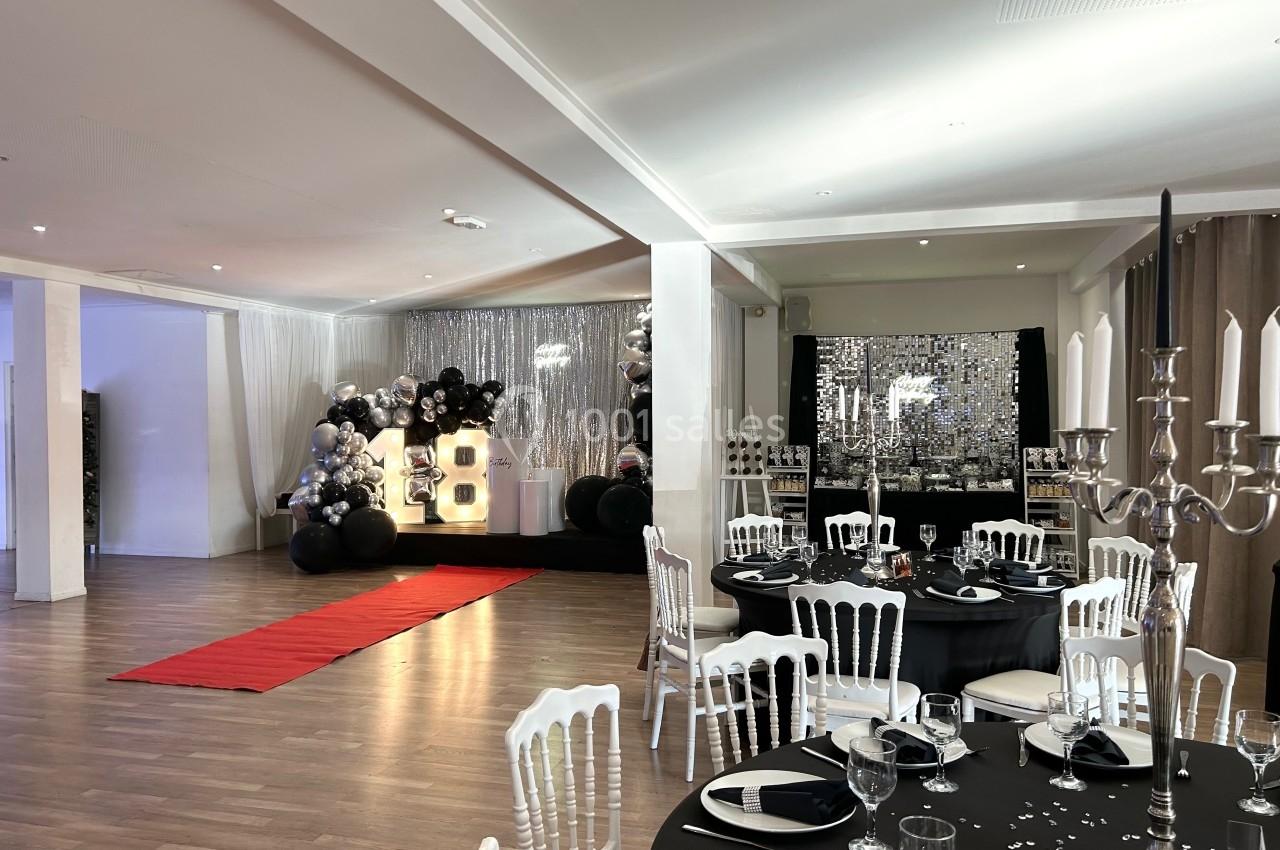 Salle décorée pour un événement avec tables dressées, tapis rouge et décor lumineux incluant le chiffre 18.