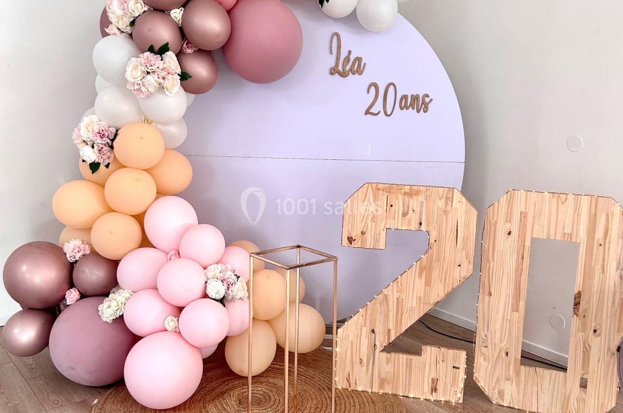 Décoration d'anniversaire avec arche de ballons pastel, panneau ’Léa 20 ans’ et chiffres en bois sur un tapis rond.