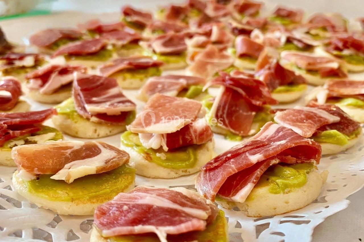 Assortiment de canapés garnis de jambon cru et d'une base de crème verte, disposés sur un plateau décoratif.