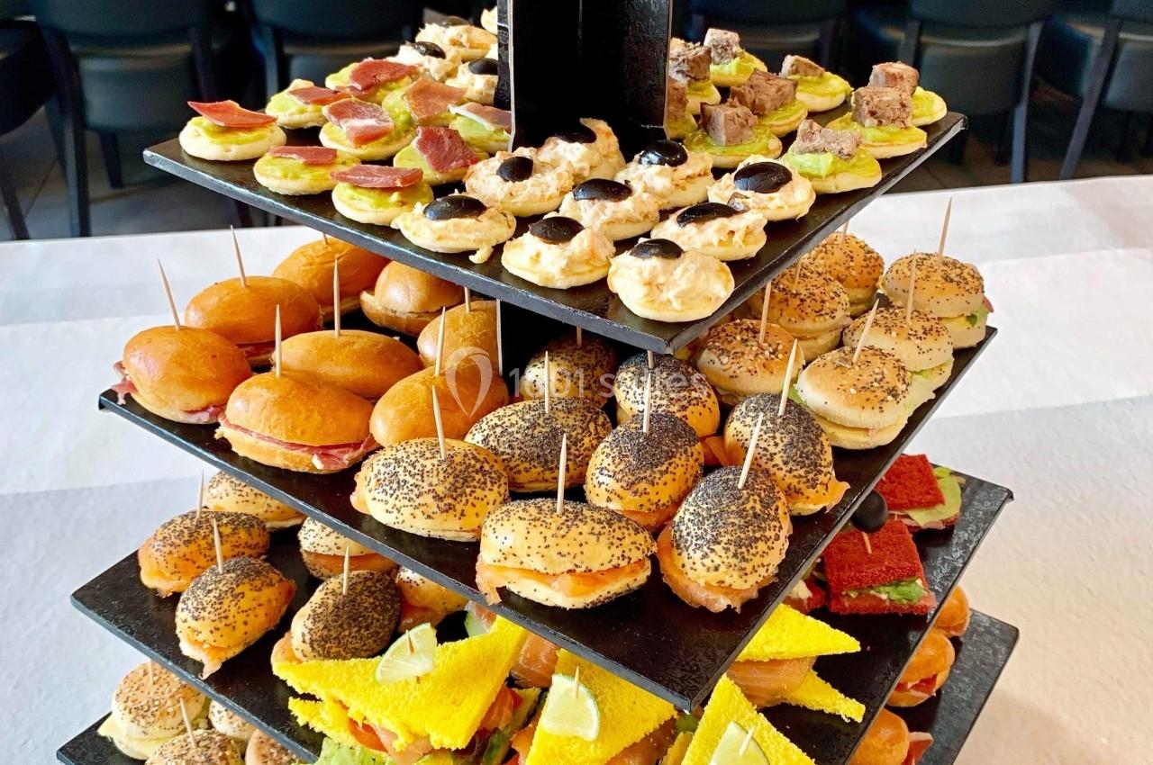 Plateau à étages présentant une variété de petits sandwichs et amuse-bouches colorés sur une table blanche.