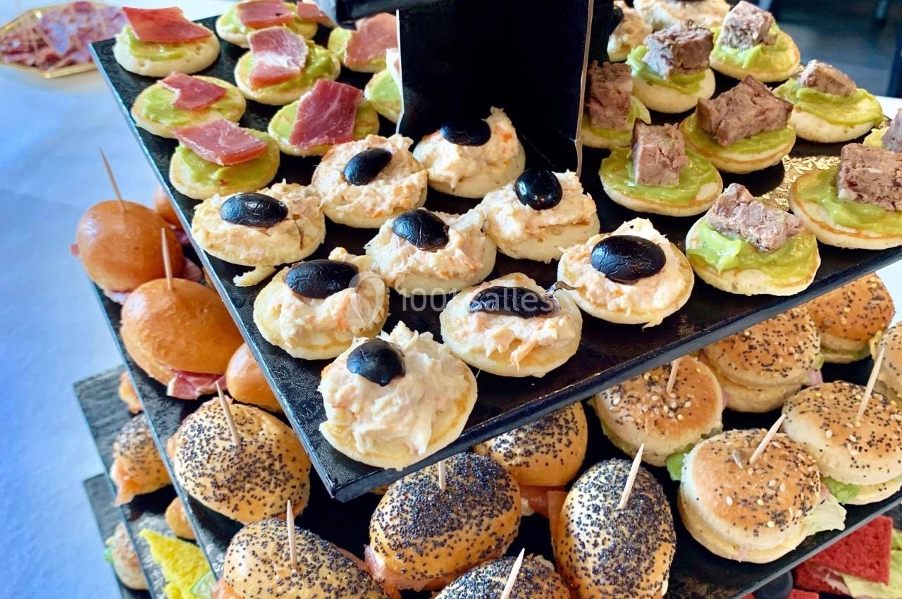 Plateau de bouchées apéritives variées disposées sur plusieurs étages, comprenant canapés, mini-burgers et toasts colorés.