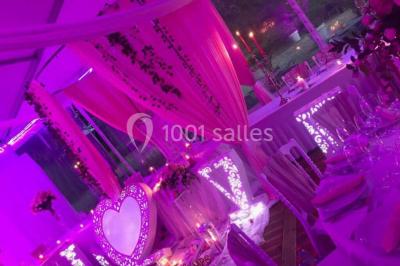 Décoration de salle de réception avec éclairage rose, rideaux, chandeliers et ornements lumineux en forme de cœur.