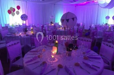 Décoration de salle de réception avec éclairage rose, rideaux, chandeliers et ornements lumineux en forme de cœur.